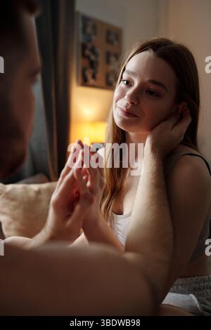 Couple romantique profitant d'un moment doux ensemble dans une pièce chaleureusement éclairée avec une atmosphère chaleureuse. Femme regardant avec amour le partenaire tout en se tenant les mains et embrassant la proximité Banque D'Images