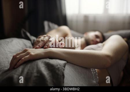L'homme dort paisiblement dans son lit pendant la journée avec une expression sereine. La lumière du soleil qui traverse la fenêtre met en valeur l'atmosphère calme de la pièce Banque D'Images