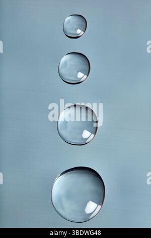 Gouttelettes d'eau disposées verticalement sur une surface lisse bleu clair. Banque D'Images