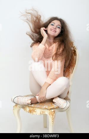 Heureuse jeune femme assise sur une chaise ornée, ses longs cheveux attrapèrent à mi-mouvement Banque D'Images