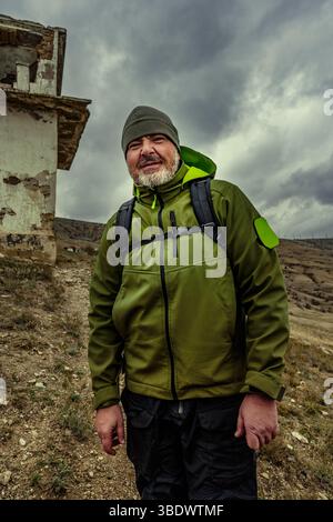 Randonneur se tient en toute confiance près d'un bâtiment abandonné contre un ciel nuageux spectaculaire dans une région montagneuse Banque D'Images