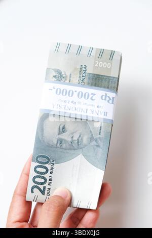 Pekanbaru, Indonésie - 21 mars 2025 : main tenant des billets de banque rupiah indonésiens RP 2,000 isolés sur fond blanc pour THR sur Eid al-Fitr ou Lebara Banque D'Images