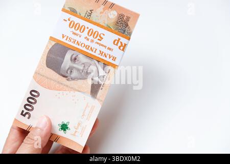 Pekanbaru, Indonésie - 21 mars 2025 : main tenant des billets de banque rupiah indonésiens RP 5,000 isolés sur fond blanc pour THR sur Eid al-Fitr ou Lebara Banque D'Images