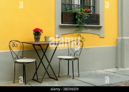 Des chaises et une table sont posées contre le mur jaune dans un restaurant en plein air dans la vieille ville d'Alba, en Italie. Banque D'Images