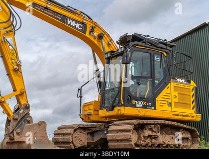 Vue latérale rapprochée d'une pelle mécanique JCB au repos devant un bâtiment agricole en acier, Royaume-Uni avec un ciel nuageux au-dessus. Banque D'Images