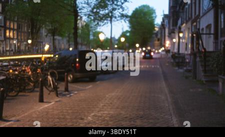 Le paysage urbain floue d'une ville européenne présente des lampadaires bokeh, des arbres floues, des vélos, des voitures et des rues pavées créant un U serein Banque D'Images
