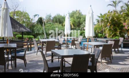 Scène de villégiature de luxe en plein air floue avec fond tropical défocalisé avec chaises en osier vides et parasols installés sur un patio en bois, évoquant un Banque D'Images
