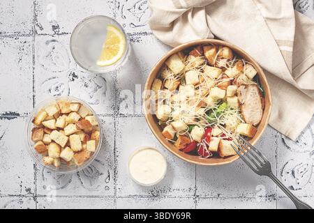 Salade César dans un récipient en papier, prenez-la sur le chemin, avec de la sauce et des croûtons, sur la table, collation, lumière naturelle, pas de gens Banque D'Images