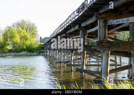 Un charmant pont piétonnier en bois s'étend sur la rivière, ses planches altérées offrant un chemin rustique à travers la nature. Le flux serein du ri Banque D'Images