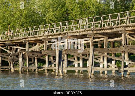 Un charmant pont piétonnier en bois s'étend sur la rivière, ses planches altérées offrant un chemin rustique à travers la nature. Le flux serein du ri Banque D'Images