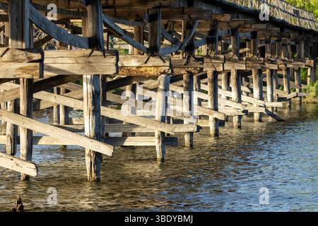 Un charmant pont piétonnier en bois s'étend sur la rivière, ses planches altérées offrant un chemin rustique à travers la nature. Le flux serein du ri Banque D'Images