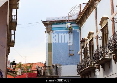 Guanajuato City, Mexique - 30 mai 2016 : un ouvrier de la construction est sur une échelle peignant le flanc d'un bâtiment à Guanajuato City, Mexique. Banque D'Images