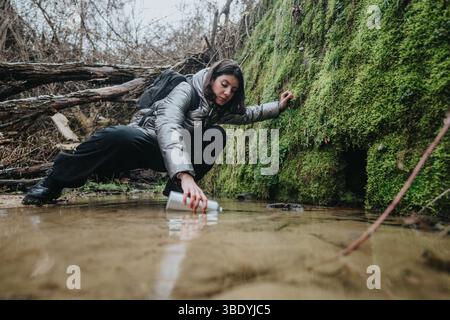 Femme recueillant l'échantillon d'eau de Clear Stream dans l'environnement forestier Banque D'Images