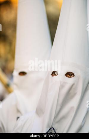 Nazaréens portant des capuchons blancs se tiennent solennellement pendant les célébrations de la semaine Sainte à Séville, reflétant les traditions culturelles profondes de l'événement. Banque D'Images