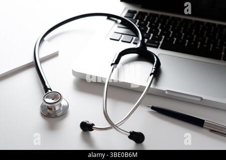 Gros plan sur le lieu de travail du médecin avec un stéthoscope, un ordinateur portable, un cahier et un stylo. Banque D'Images