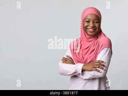Femme noire souriante dans le hijab posant sur le gris Banque D'Images
