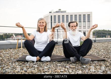 Couple plus âgé pratiquant le yoga en plein air dans la pose de lotus sur le toit urbain Banque D'Images