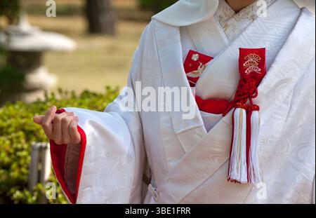 Mariée japonaise portant un kimono blanc traditionnel 'shiromuku' avec accessoire de bon augure comme un 'omamori' (pochette de protection) au Japon. Banque D'Images