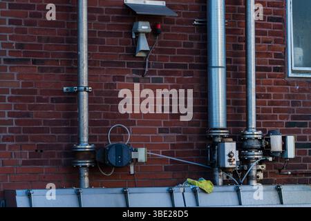 Des tuyaux métalliques et divers équipements sont installés sur un mur de briques rouges. Le cadre semble industriel, sans activité humaine visible. La configuration Banque D'Images