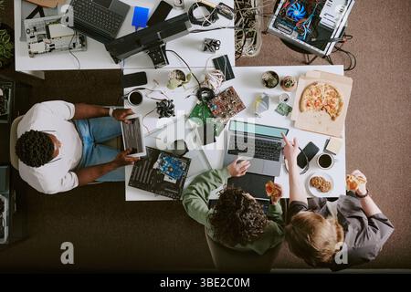 Groupe de personnes discutant à l'espace de travail encombré avec divers appareils électroniques. Les membres de l'équipe analysent et partagent des idées, s'engagent dans la collaboration Banque D'Images