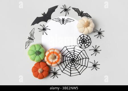 Composition d'Halloween de citrouilles tricotées orange et vertes, de toiles d'araignée noires et d'araignées et de chauves-souris avec un endroit blanc rond pour le texte. Jouets tricotés faits à la main pour enfants et décoration de maison de vacances. Banque D'Images