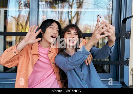 De jeunes amis joyeux partagent un moment joyeux en prenant des selfies ensemble dans un café animé. Banque D'Images