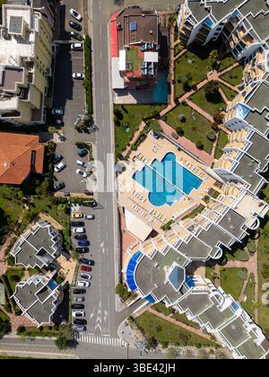 Vue aérienne de haut en bas d'un complexe résidentiel moderne avec piscine, chaises longues, jardins paysagers et bâtiments environnants. Journée ensoleillée Banque D'Images