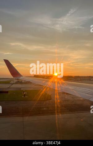 Une aile d'avion est vue au premier plan d'un coucher de soleil. Le soleil se couche en arrière-plan, projetant une lueur chaude sur la scène. Concept de calme et tran Banque D'Images