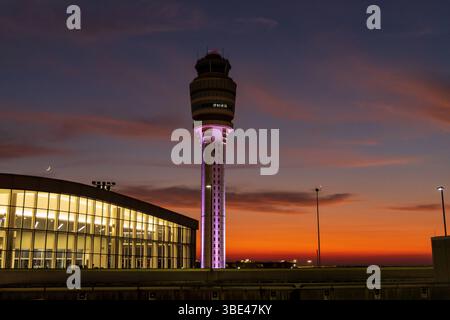 Un grand terminal d'aéroport avec une grande tour en arrière-plan. Le ciel est orange et le soleil se couche Banque D'Images