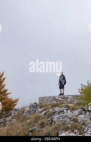 L'homme se tient en toute confiance au sommet de la plate-forme circulaire en pierre surplombant la forêt de montagne d'automne brumeuse. Banque D'Images
