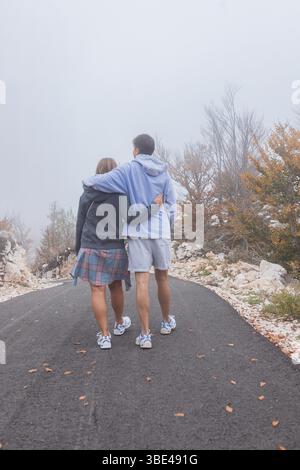 Jeune couple embrassant sur le chemin brumeux à travers les bois d'automne Banque D'Images