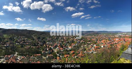 Un large panorama capturant une ville pittoresque nichée au milieu de collines vibrantes sous un ciel ensoleillé. Cette scène en grand angle met en valeur un feuillage luxuriant, des toits rouges, un Banque D'Images