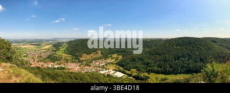 Un paysage panoramique à couper le souffle mettant en valeur un village pittoresque, entouré de collines verdoyantes sous un ciel bleu vibrant. Une représentation parfaite de Ser Banque D'Images