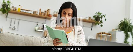 Dans un cadre intérieur serein, une femme enceinte se concentre sur son journal tout en étant assise confortablement. Banque D'Images