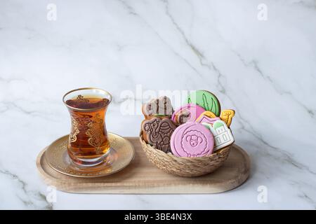 Thé traditionnel dans un verre doré servi avec des biscuits colorés au pain d'épice sur le thème de l'Eid dans un panier. Gâteau de fête parfait pour la fête du Qurban Bayram Banque D'Images