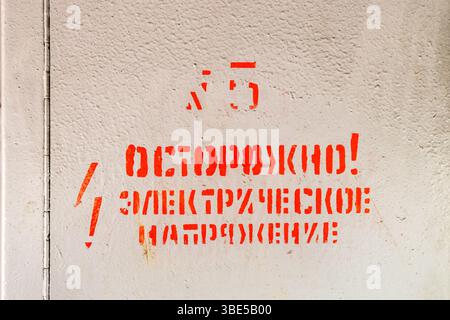 Panneau de peinture rouge attention ! Tension électrique sur russe sur la porte fermée du boîtier électrique Banque D'Images