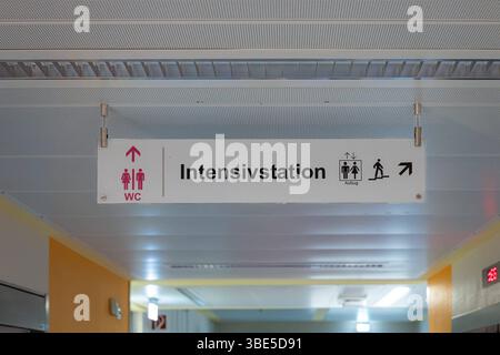 Deutschland 25. Avril 2025 : Im Bild : Ein klarer und funktionaler, von der Decke abgehängter Wegweiser ist in einem Krankenhausflur. DAS Schild zeigt Richtungen zu wichtigen Bereichen an : WC mit einem Piktogramm und einem Pfeil nach oben, Intensivstation in der Mitte, und Aufzug mit Piktogrammen für Treppen und Personen sowie einem Pfeil, der nach rechts und oben zeigt. Die Beleuchtung des flurs mit gelblichen Akzenten trägt zur Orientierung BEI. Dieses Foto eignet sich hervorragend für Beiträge über das Gesundheitswesen, Krankenhäuser, Kliniken, Patientenführung, Beschilderung, navigation en g Banque D'Images