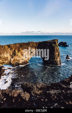 Vue sur une magnifique arche marine naturelle contre l'immense océan bleu en Islande. La formation rocheuse est haute avec des vagues qui rodent à sa base, sous Banque D'Images