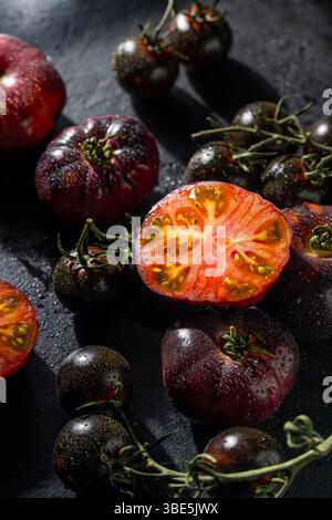 Gros plan de tomates anciennes colorées, entières et coupées en deux, avec des gouttelettes d'eau. Les textures riches et les couleurs éclatantes contrastent magnifiquement avec Banque D'Images