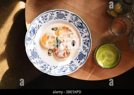 Vue de dessus d'un cadre de petit-déjeuner composé de crêpes au fromage cottage servies sur une assiette décorative bleue et blanche, accompagnée d'un verre de vert matcha Banque D'Images