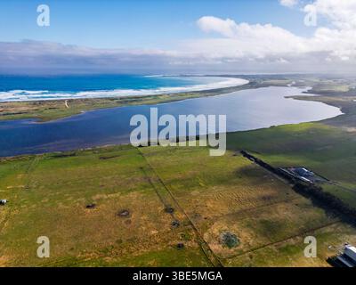 Une vue aérienne époustouflante capture un lac côtier se fondant parfaitement dans l'océan sous un ciel clair, avec des champs verdoyants entourant la région, offe Banque D'Images