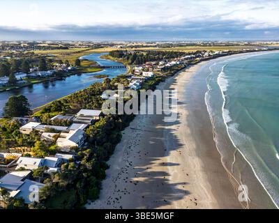 Une vue aérienne panoramique met en valeur un village côtier flanqué d'une plage de sable et d'une rivière paisible, soulignant le mélange harmonieux de beauté naturelle et Banque D'Images