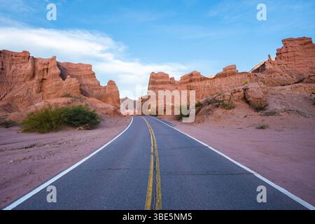 Une route pittoresque courbe entre des formations rocheuses rouges spectaculaires sous un ciel clair dans le désert aride de la Puna, Argentine, mettant en valeur la beauté unique de Banque D'Images