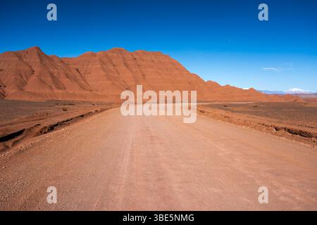 Une vue imprenable sur une route poussiéreuse éloignée qui s'étend à travers le paysage aride de la Puna, en Argentine, flanquée de grandes collines brunes sous un bleu vif Banque D'Images