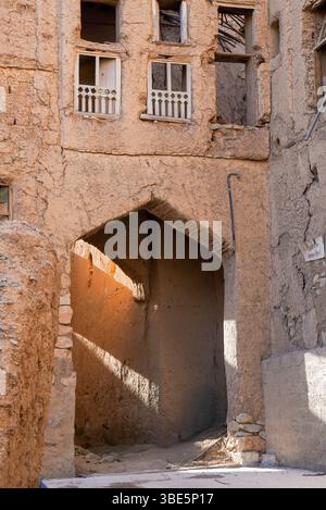 Une arche texturée éclairée par le soleil jette des teintes dorées sur les façades en ruines des bâtiments traditionnels en brique de boue à Al Hamra, Oman, mettant en valeur l'histoire Banque D'Images