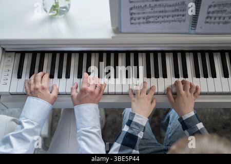 Vue rapprochée de mains adultes et enfants jouant du piano ensemble, mettant l'accent sur l'apprentissage et l'enseignement de la musique. Une belle scène d'harmonie et de connectio Banque D'Images