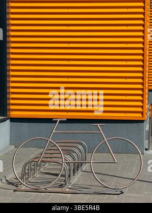 Architecture industrielle moderne avec un mur en métal orange vif et un porte-vélos conçu de manière créative en forme de vélo. Banque D'Images