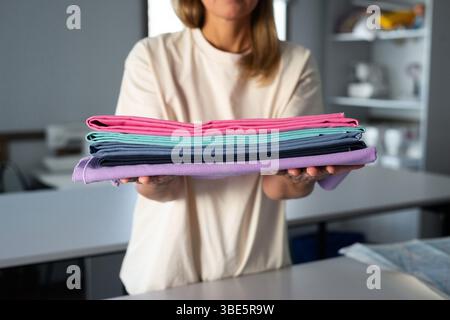 Une femme dans un atelier de couture tient des tissus colorés soigneusement pliés. L'image capture l'essence de la créativité et de l'artisanat, avec des tissus en vib Banque D'Images