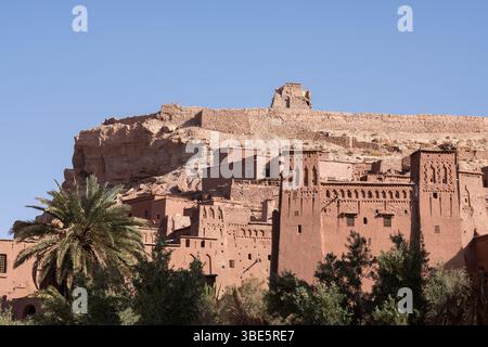 Une kasbah marocaine traditionnelle située contre un paysage désertique rocheux du ksar d'ait Ben Haddou. Les structures en argile et les palmiers luxuriants créent un strikin Banque D'Images