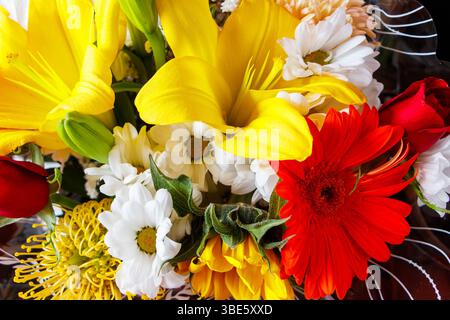Bouquet vibrant de fleurs assorties comprenant des lis, des marguerites, des gerbera et des roses dans des couleurs vives jaune, rouge et blanc Banque D'Images